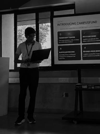 A presenter holding a laptop stands beside a large screen showing a slide titled Introducing CampusFund.