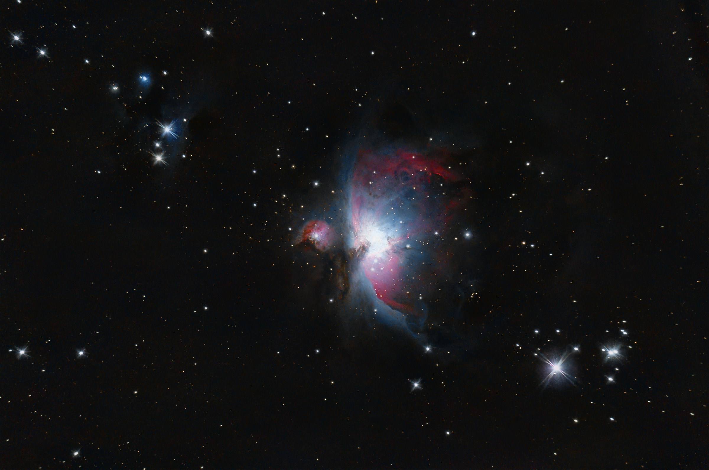 The Orion Nebula: a bright blue-white core with wings of pink gas, among scattered blue stars.