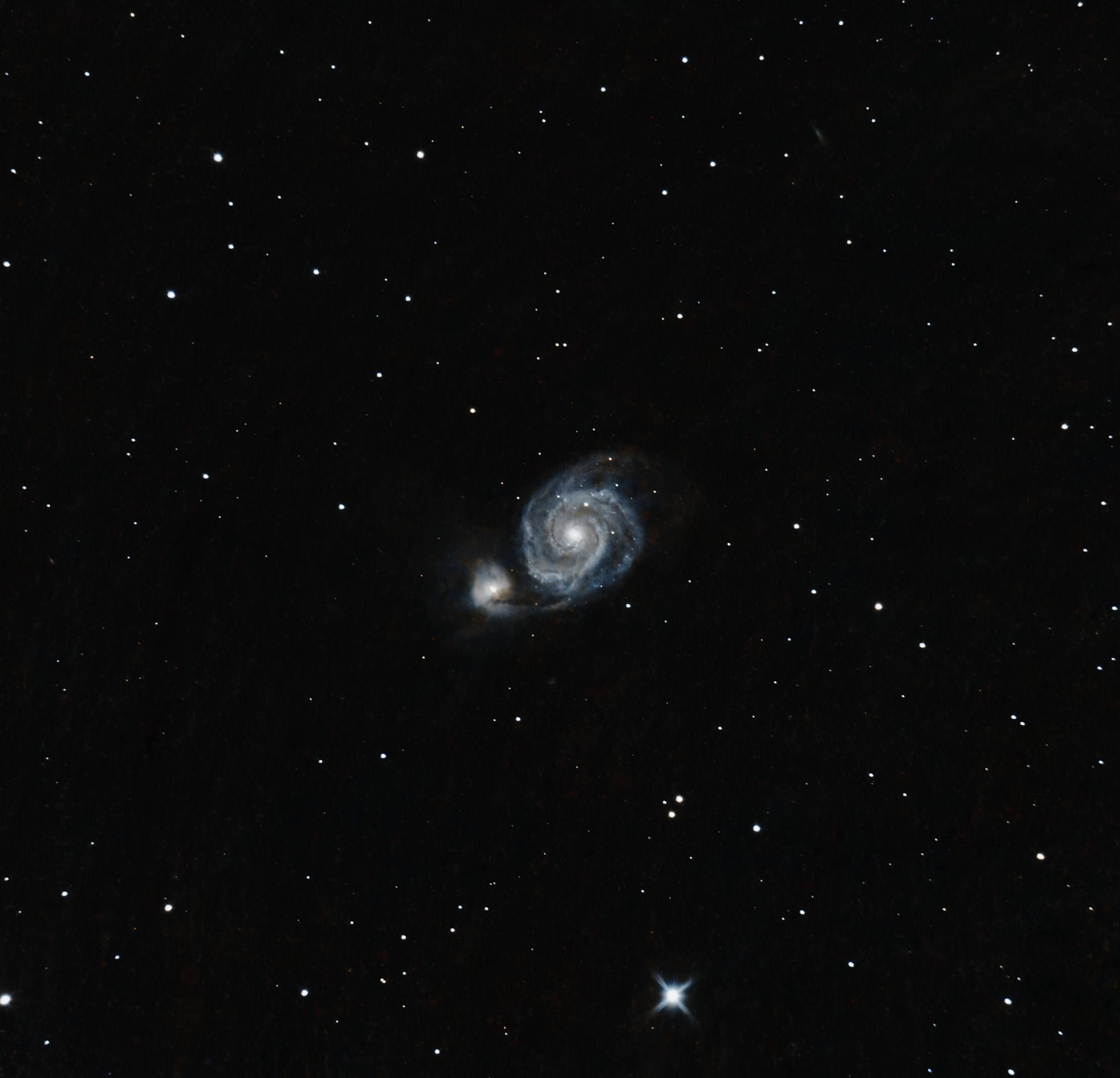 The Whirlpool Galaxy: a small face-on spiral with a companion galaxy beside it, in a field of stars.